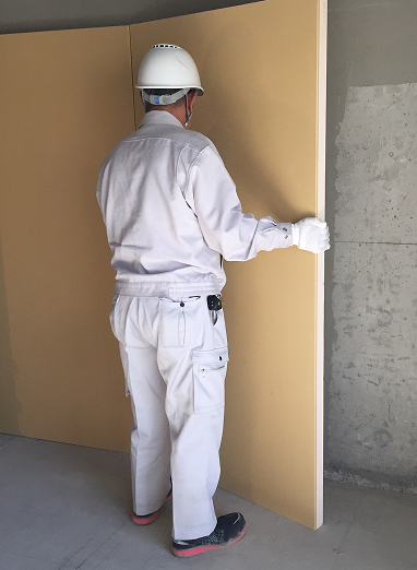 カネライトパネルを壁に貼り付けようとしている現場作業員