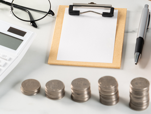 白い机に並べられた小銭と電卓、眼鏡にメモ帳とペン