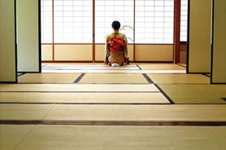 畳が敷かれた和室に正座して背を向けている和装の女性