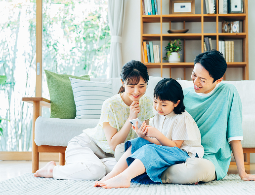 リビングで同じスマートフォンを見ている夫婦と娘の図