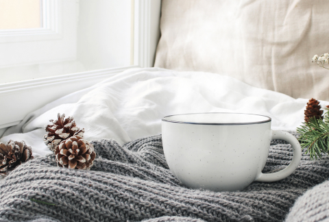 毛糸で作られたベッドカバーの上に松ぼっくりと白いマグカップが置かれた寝室